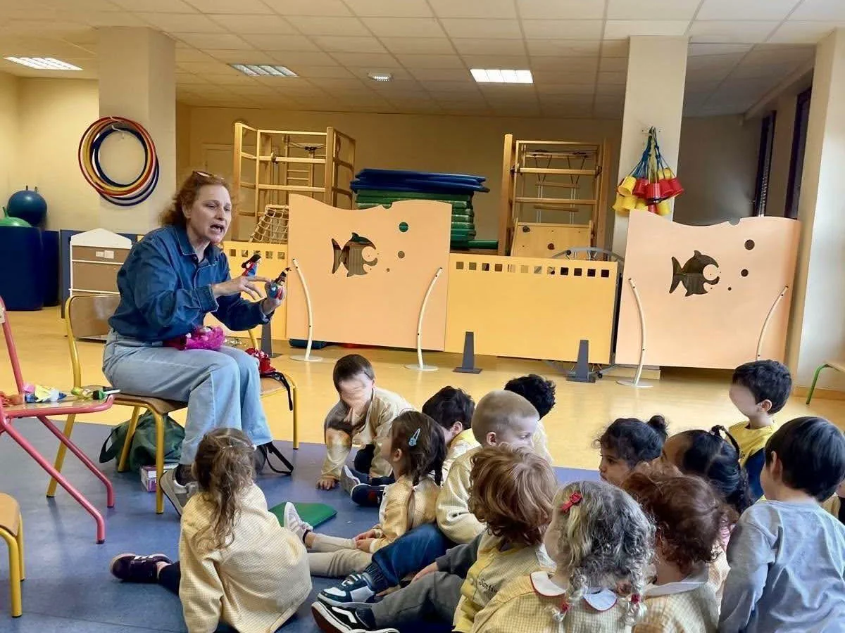 Élodie Tisserand, assise avec une marionnette à la main, raconte un opéra à un groupe d'enfants assis devant elle dans la salle de motricité d'une école maternelle.